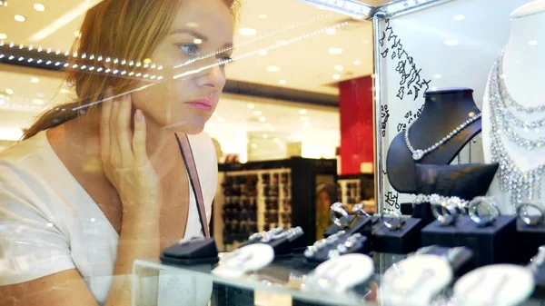 Close-up, woman looks at jewelry through a glass showcase. — Stock Photo, Image
