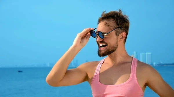 Gros plan, beau gosse ludique en t-shirt rose sur une plage tropicale. il regarde la caméra, se réjouit et fait des grimaces drôles — Photo
