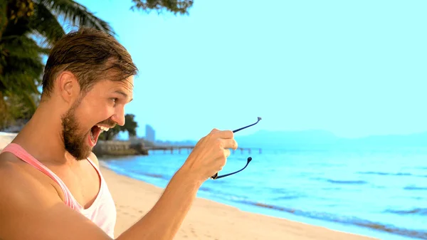 Close-up, Bonitão brincalhão com t-shirt cor-de-rosa numa praia tropical. ele olha para a câmera, se alegra e faz caras engraçadas — Fotografia de Stock