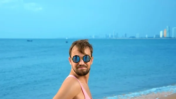 Close-up, Bonitão brincalhão com t-shirt cor-de-rosa numa praia tropical. ele olha para a câmera, se alegra e faz caras engraçadas — Fotografia de Stock