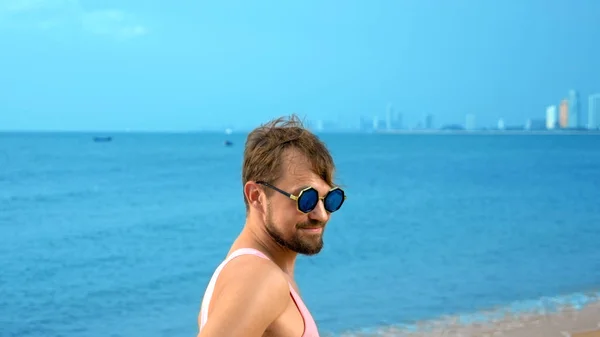 Close-up, Bonitão brincalhão com t-shirt cor-de-rosa numa praia tropical. ele olha para a câmera, se alegra e faz caras engraçadas — Fotografia de Stock