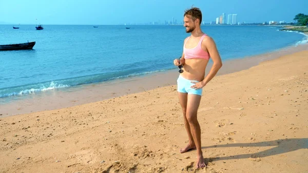 Chico guapo juguetón en una camiseta rosa y pantalones cortos azules se regocija en la playa. monstruo en el mar . — Foto de Stock