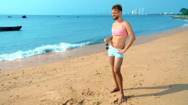 Chico guapo juguetón en una camiseta rosa y pantalones cortos azules se regocija en la playa. monstruo en el mar . — Foto de Stock