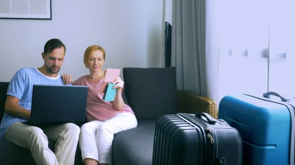 Tourismuskonzept, Online-Shopping-Touren. romantisches Paar, das sich auf eine Reise zu Hause vorbereitet. Mit Laptop und Reisepass in der Hand auf der Couch sitzen. während die Koffer in der Nähe sind, konzentrieren Sie sich auf die — Stockfoto