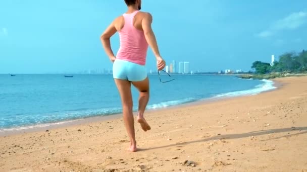 Giocoso bel ragazzo in una t-shirt rosa e pantaloncini blu gioisce in spiaggia. mostro sul mare . — Video Stock