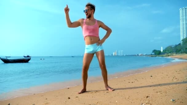 Giocoso bel ragazzo in una t-shirt rosa e pantaloncini blu gioisce in spiaggia. mostro sul mare . — Video Stock