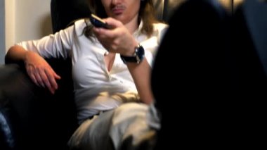 kanepede oturan ve Tv kanallarını kontrol panelinden anahtarlama yüzünde boyalı bıyıklı çift cinsiyetli bir feminist portresi