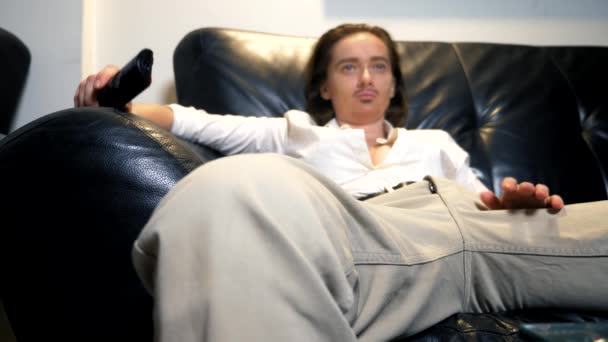 Πορτρέτο του ένα ανδρόγυνο φεμινίστρια με ένα ζωγραφισμένο μουστάκι στο πρόσωπό της, κάθεται στον καναπέ και μεταγωγής τηλεοπτικά κανάλια από τον πίνακα ελέγχου — Αρχείο Βίντεο