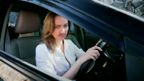 Un retrato de una feminista andrógina con un bigote pintado en la cara sentada al volante de un coche. mujer mira a la cámara desde la ventana del coche . — Vídeos de Stock