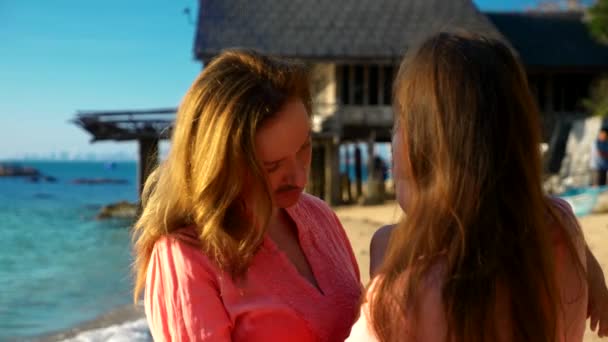 El concepto de las extrañas aventuras de la gente. Feliz pareja lesbiana con bebé caminando en la hermosa playa tropical. una de las mujeres con bigote en la cara como símbolo de emancipación . — Vídeos de Stock