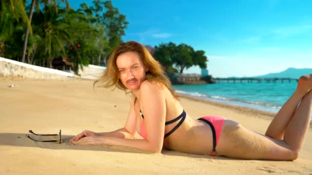 Le concept des aventures étranges des gens. Une belle femme en bikini rose sur la plage, tournée vers la caméra, et sa moustache est visible sur son visage .