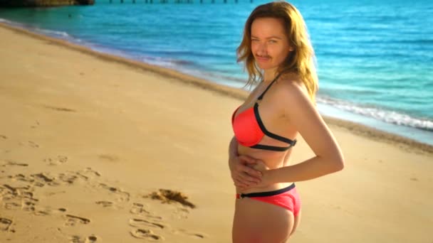 The concept of strange adventures of people. A beautiful woman in a pink bikinis on the beach, turned to the camera, and her mustache is visible on her face. — Stock Video
