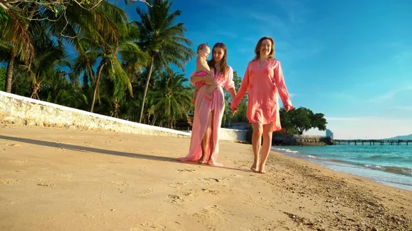 The concept of the strange adventures of people. Happy lesbian couple with babe walking on beautiful tropical beach. one of the women with a mustache on her face as a symbol of emancipation.