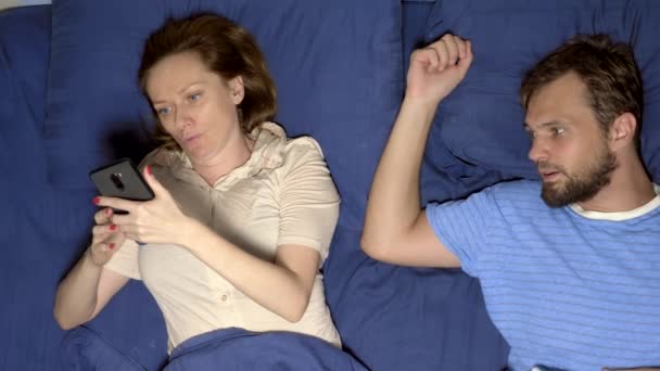 Koncepcja problem w seks. para w łóżku. mąż jest zdenerwowany, podczas gdy jego żona jest za pomocą telefonu komórkowego, ignorując go w relacji — Wideo stockowe