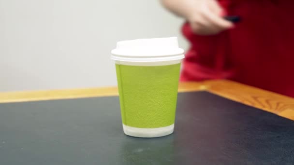 Eine Frau im roten Kleid nimmt eine Tasse Kaffee aus Pappe und legt Lipgloss daneben. — Stockvideo