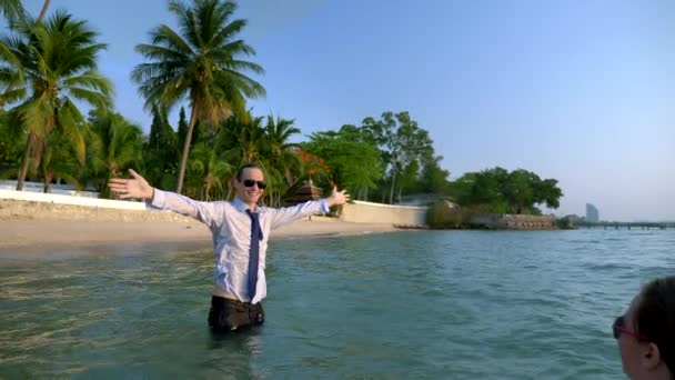 Feliz pareja mujer de negocios y hombre de negocios en traje y gafas de sol salpicando en el mar en resorts de lujo. El concepto de unas vacaciones tan esperadas, freelancing . — Vídeos de Stock