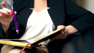 yakın çekim. bir kadın akşam ofiste bir siyah deri sandalyede otururken bir defterde notlar alır. Danışma, müzakere, kavramı planlama