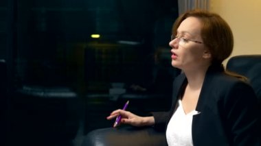 yakın çekim. bir kadın biriyle konuşuyor ve akşam ofiste bir siyah deri sandalyede otururken bir defterde notlar alır. Danışma, müzakere kavramı.