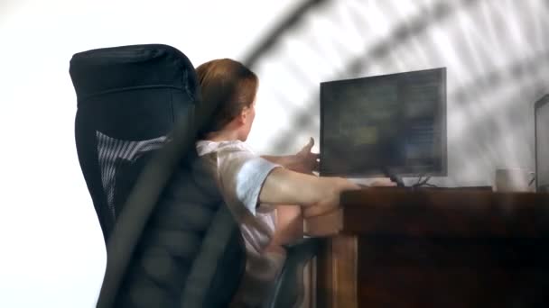 Nahaufnahme eines Teils eines Büroventilators, auf dem Hintergrund eines verschwommenen Schreibtisches, an dem eine Person am Computer arbeitet — Stockvideo