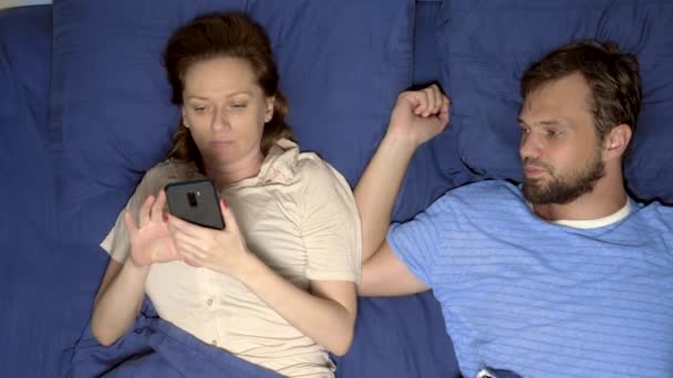 Conceito de um problema no sexo. casal na cama. marido está chateado enquanto sua esposa está usando um telefone celular, ignorando-o em um relacionamento. vista superior — Vídeo de Stock