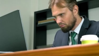 bir takım elbiseli bir adam bir dizüstü bilgisayarda ofiste bir masada çalışır ve tek kullanımlık bardak kahve içecek. Kopyalama alanı