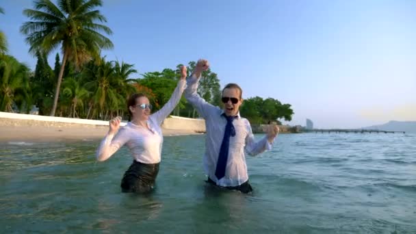 Feliz pareja mujer de negocios y hombre de negocios en traje y gafas de sol salpicando en el mar en resorts de lujo. El concepto de unas vacaciones tan esperadas, freelancing . — Vídeo de stock