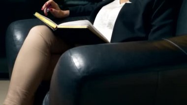 yakın çekim. bir kadın biriyle konuşuyor ve akşam ofiste bir siyah deri sandalyede otururken bir defterde notlar alır. Danışma, müzakere kavramı.