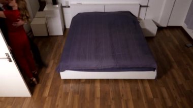 Takım elbiseli bir erkek ve bir kadın kırmızı tulum içinde yatak odası ve öpücük girin. sarılmak ve birlikte yatağa düşmek