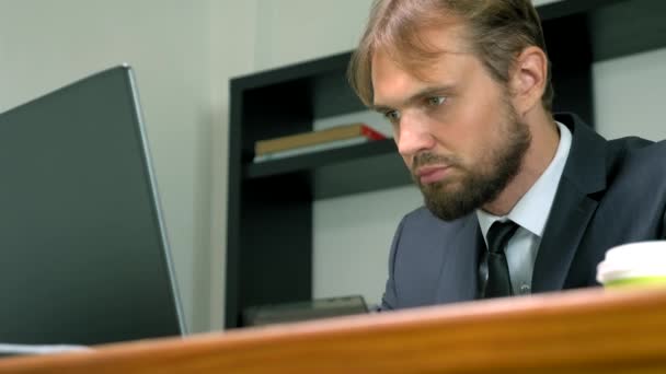 Un homme en costume travaille à un bureau dans le bureau sur un ordinateur portable et boit du café dans une tasse jetable. espace de copie — Video