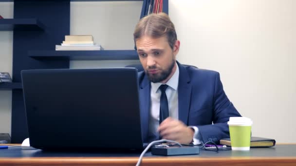 Un homme en costume travaille à un bureau dans le bureau sur un ordinateur portable et boit du café dans une tasse jetable. espace de copie — Video