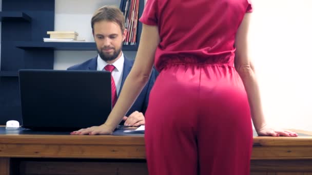 Office flirt. Aantrekkelijke vrouw in een rode jumpsuit, flirten aan de tafel met haar collega. — Stockvideo