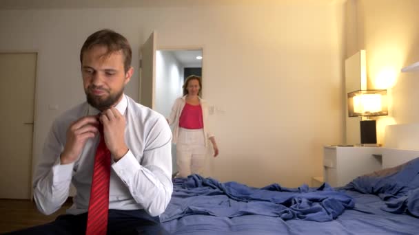 Unavený muž, sedící na posteli po pracovním dni. Atraktivní okouzlující svůdná žena vstoupí do ložnice a šeptá příjemná slova její ospalá unavená muže. — Stock video