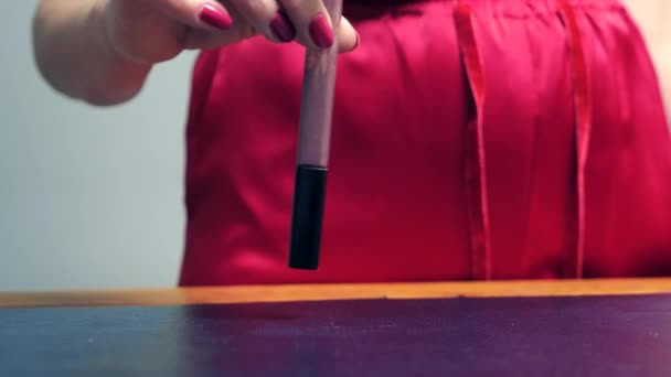 長い赤い爪を持つ女性の手は、リップグロスチューブでテーブルをノックします. — ストック動画