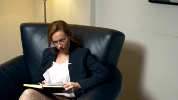 特写。晚上, 一个女人坐在办公室的黑色皮椅上, 在笔记本上和别人说话, 然后做笔记。协商、谈判的概念. — 图库视频影像