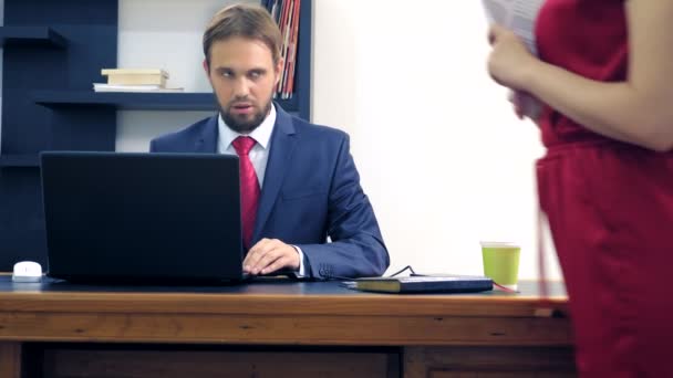 Office flirt. Attractive woman in red overalls with a deep neckline flirting at the table with her colleague. man looks at the chest of a woman in the office — Stock Video