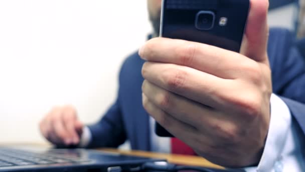 Primo piano. Uomo d'affari che utilizza smartphone mobile e sorridente, mentre lavora sul computer portatile in ufficio . — Video Stock