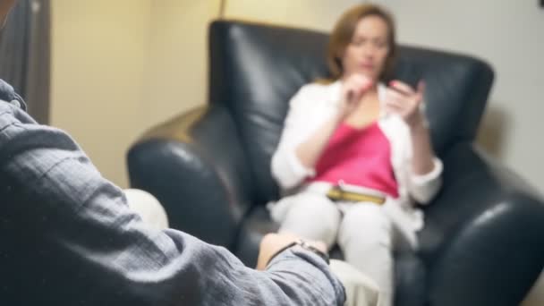 Conceptul de negociere. O femeie cu un telefon în mână comunică cu un bărbat. Seara stăteam în birou într-un scaun din piele. tastarea unui mesaj pe un smartphone în timp ce vorbiți — Videoclip de stoc