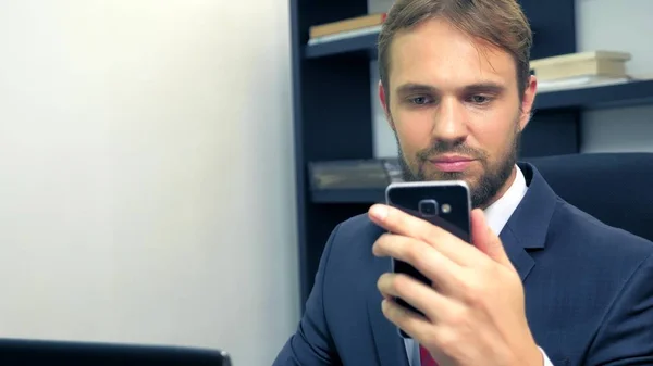 Close-up. Businessman using mobile smartphone and smiling, while working on laptop computer in office. — Stock Photo, Image
