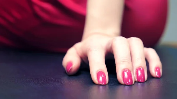 A hosszú, piros körmökkel rendelkező női kezek kopogtatnak az asztalon. Egy nő egy piros JumpSuit ül egy asztalon, és várja. — Stock Fotó