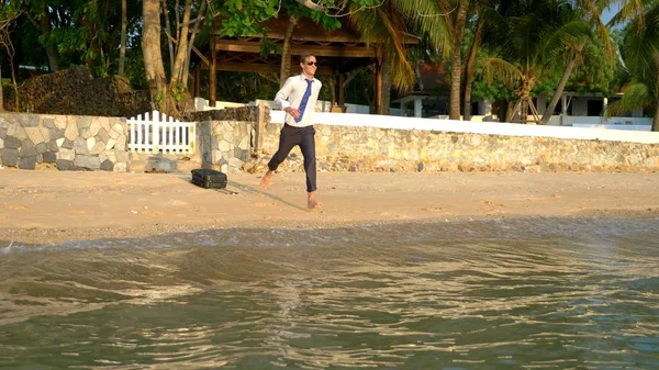 Der glückliche Geschäftsmann im Anzug und mit dunkler Brille plantscht in Luxusresorts im Meer. Konzept des lang ersehnten Urlaubs, Freelancing. — Stockfoto