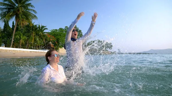 Feliz pareja mujer de negocios y hombre de negocios en traje y gafas de sol salpicando en el mar en resorts de lujo. El concepto de unas vacaciones tan esperadas, freelancing . — Foto de Stock