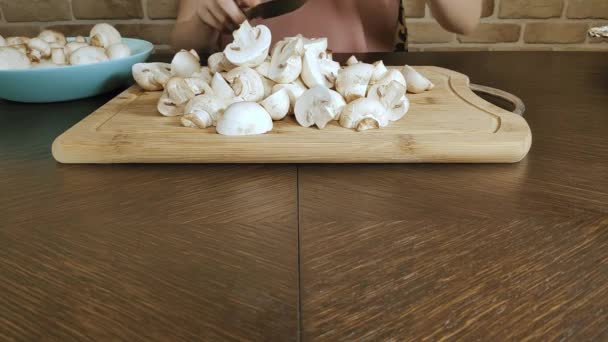 Женщина дома на кухне режет грибы на деревянной доске, крупным планом — стоковое видео