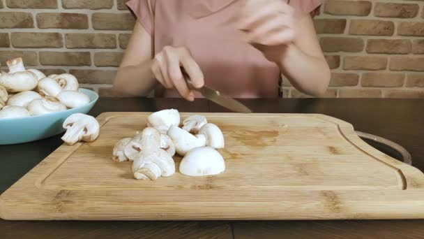 Mulher em casa em sua cozinha corta cogumelos em uma tábua de madeira, close-up — Vídeo de Stock