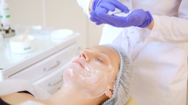 Koncept kosmetolog. Händerna på en kosmetolog sätta grädde på ansiktet av en kvinna. Kosmetolog applicerar en kräm på ansiktet på flickan — Stockvideo