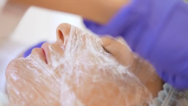 The concept of a beautician. The hands of a cosmetologist put a film on the face of a woman. anesthesia before the procedure of mesotherapy, biorevitalization or contour plastics — Stock Video