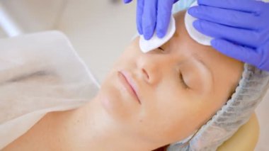 Güzellik uzmanı kavramı. Bir kozmetolojistin elleri bir kadının yüzünde pamuk ped ile losyon uygular.