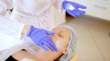 konsept güzellik. Bir kozmetolojistin elleri bir kadının yüzüne krem koyar. Güzellik kızı yüzüne bir krem uygular