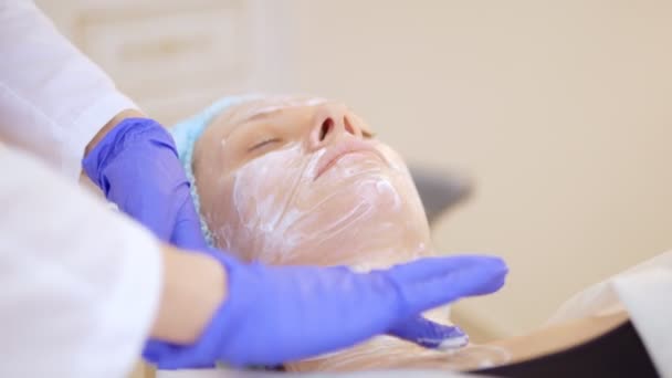 Concepto esteticista. Las manos de un cosmetólogo ponen crema en la cara de una mujer. esteticista aplica una crema en la cara de la chica — Vídeo de stock