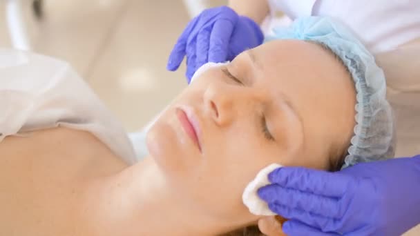 Le concept d'esthéticienne. Les mains d'un cosmétologue appliquent une lotion avec un coton sur le visage d'une femme . — Video