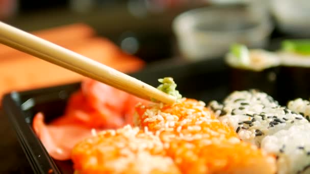 Nahaufnahme. jemand nimmt Sushi mit Stäbchen, Brötchen und Dips in Sojasauce — Stockvideo